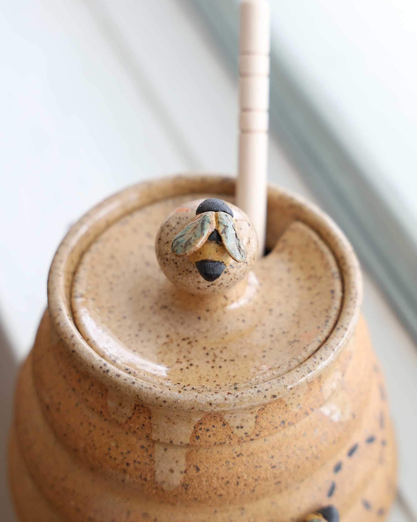 Close-up of a ceramic jar with a lid and wooden handle on a light background