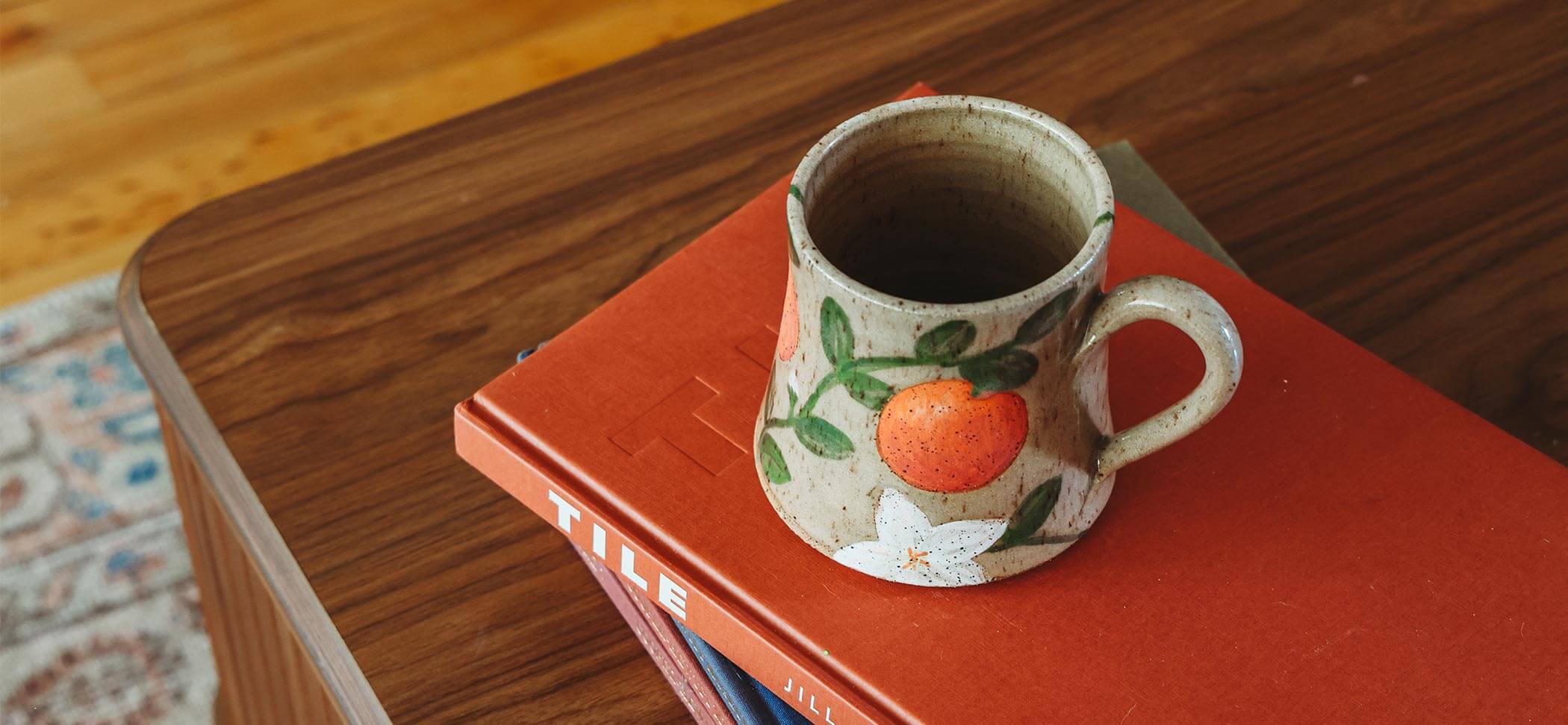 Ceramic mug with orange design on a stack of books on a wooden surface