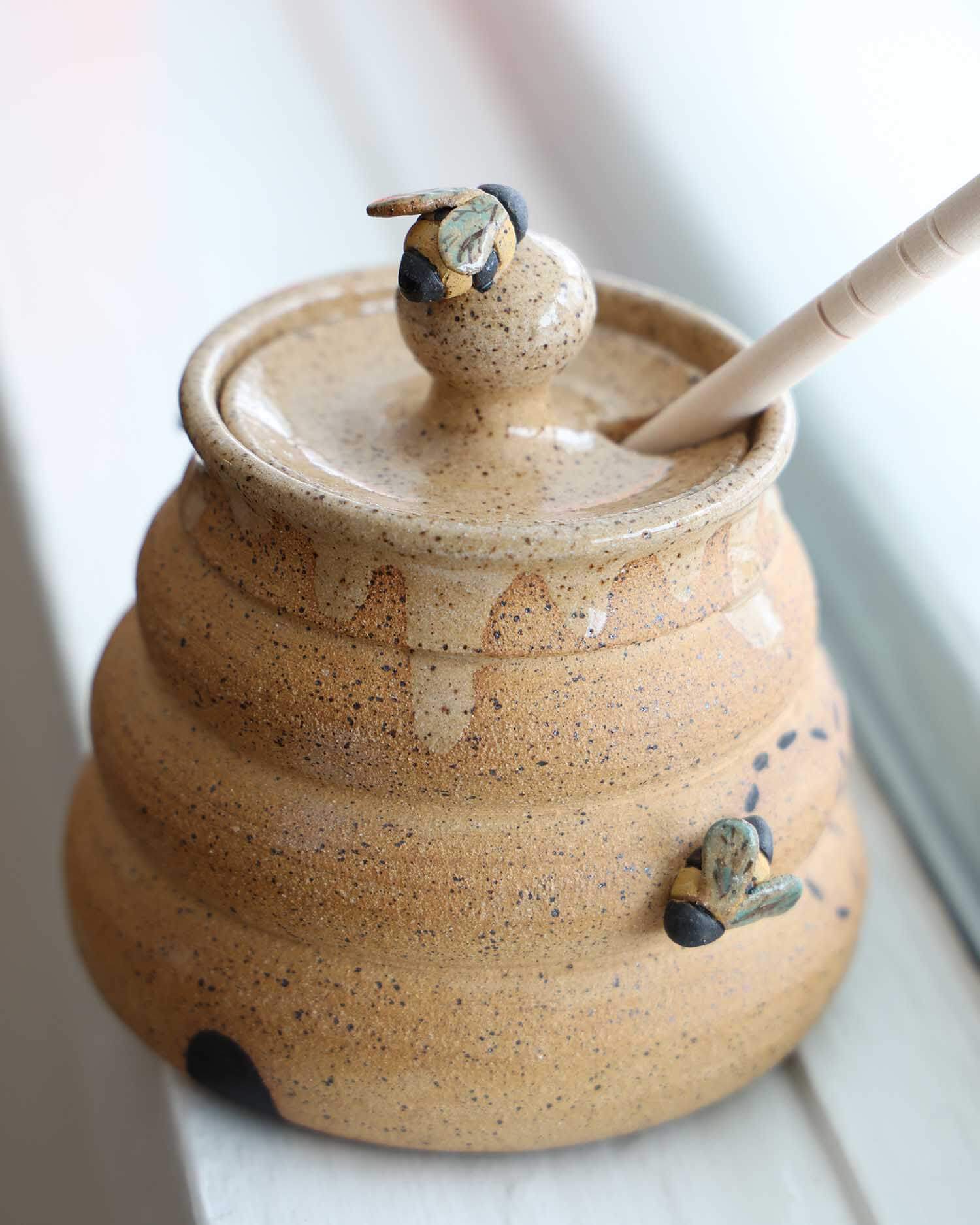 Ceramic honey pot with a lid and wooden dipper on a light background