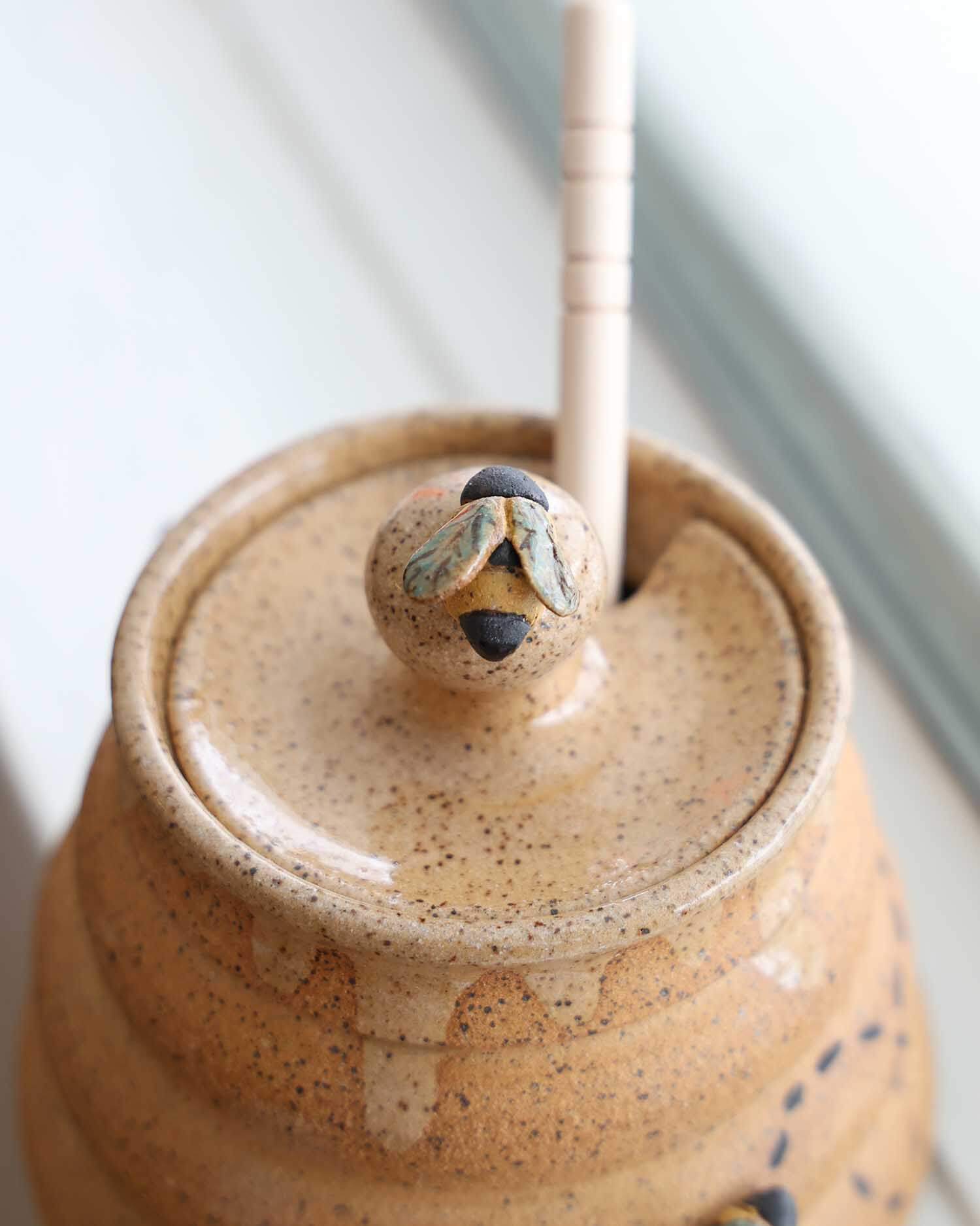Close-up of a ceramic jar with a lid and wooden handle on a light background